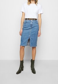 Denim pencil skirt with front slit, light blue color, high waist, paired with a plain white T-shirt and olive green ankle boots.