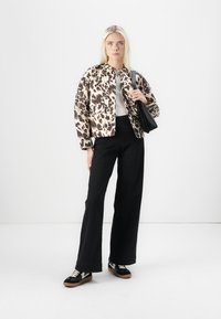 Jakna s printevom leoparda, bijela majica, crne hlače viskog struka i crne tenisice s smešnim potplatima; model drži crnu torbu.