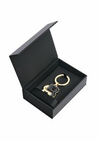 Gold keychain with a black monogrammed "B," resting on a black satin ribbon inside a black box with a lid.