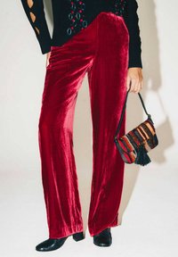 Pantaloni a gamba larga in velluto rosso abbinati a una borsa intrecciata multicolore, rifinita con un nappina nera. Scarpe con tacco nere con stampa a effetto coccodrillo.