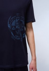 Mørkeblå bomulds T-shirt med korte ærmer, prydet med et blåt grafisk trykdesign på forsiden. Synlige syninger nær kanten.