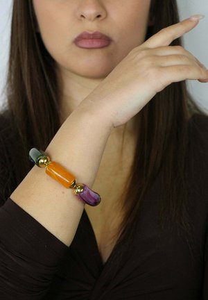 Bracelet coloré comprenant trois perles rectangulaires en orange, vert et violet avec des accents dorés sur une fine bande reposant sur un poignet.