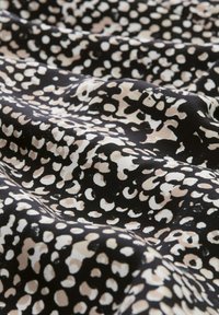 Tessuto stampato con uno sfondo nero e forme astratte color crema e beige, texture liscia, piegato con pieghe visibili.