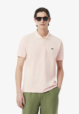 Light pink polo shirt with a classic collar, short sleeves, and a green crocodile logo on the left chest, paired with green pants.