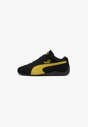 Baskets noires Puma avec bande latérale jaune, logo Puma, lacets noirs et semelle noire texturée, vues de côté sur fond blanc.