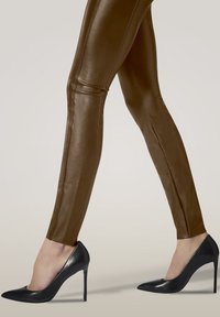 Leggings in ecopelle marrone con un design aderente, caratterizzati da dettagli delle cuciture. Abbinati a décolleté in pelle verniciata nera con tacco a stiletto e punta affusolata.