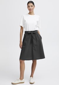 Svart midi skjørt med snor i livet, som har lommer og avslappet passform, kombinert med en enkel hvit t-skjorte med korte ermer og sneakers.