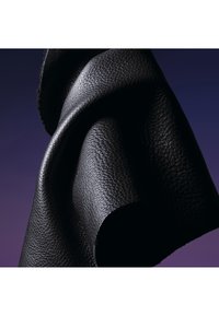 Tissu en cuir noir plié avec un motif de grain texturé sur un fond dégradé violet foncé.