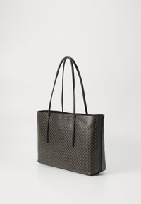 Sac fourre-tout noir avec des poignées fines, doté d'un motif géométrique doré sur un fond clair.