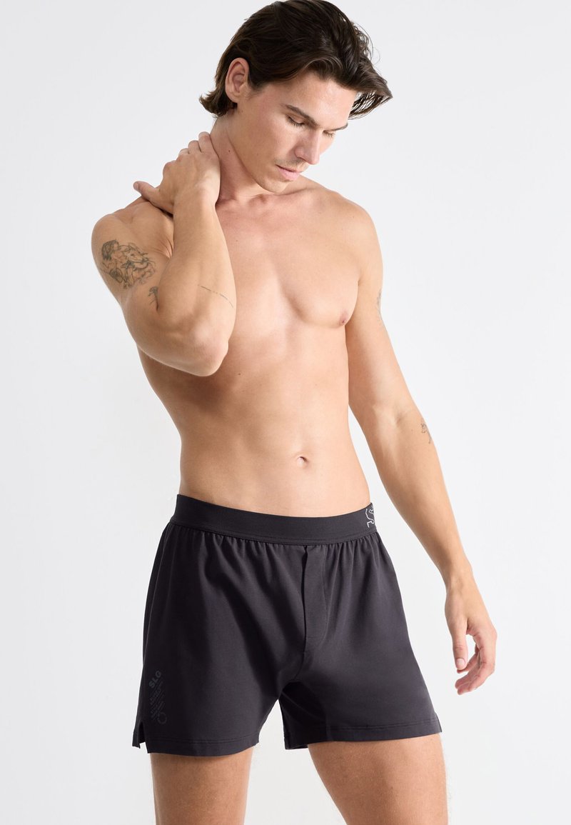 Shorts sportivi neri con elastico in vita, caratterizzati da una lieve lucentezza, fessure laterali e un branding discreto sulla gamba sinistra.