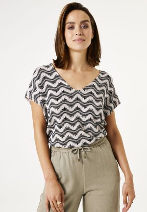 Zwart-wit geblokte blouse met een V-hals, korte mouwen en een ontspannen pasvorm, gecombineerd met lichte broek met trekkoord.