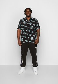 Short-sleeve black shirt with colorful floral pattern, paired with black sweatpants featuring white and purple text; white sneakers.