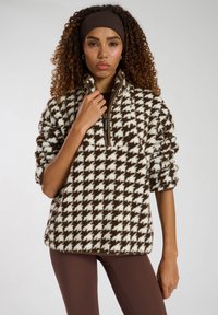 Pullover in pile con un motivo houndstooth marrone e bianco, con zip a metà, collo con bavero e polsi a costine. Texture morbida e vestibilità rilassata.