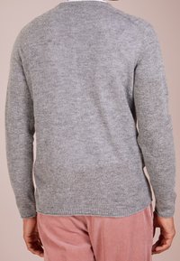 Grauer Strickpullover mit langen Ärmeln, rundem Ausschnitt und weicher Textur; getragen über pinken Cordhosen und vermittelt ein lässiges Design.