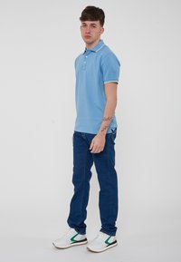 Polo shirt azzurro chiaro con maniche corte, rifiniture del colletto bianche, abbinato a jeans blu scuro e sneakers bianche con accenti verdi.