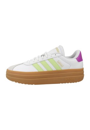 Zapatilla blanca Adidas con rayas verde claro, suela gruesa marrón, lengüeta morada en el talón y logo dorado de Adidas en la lengüeta y el lateral.