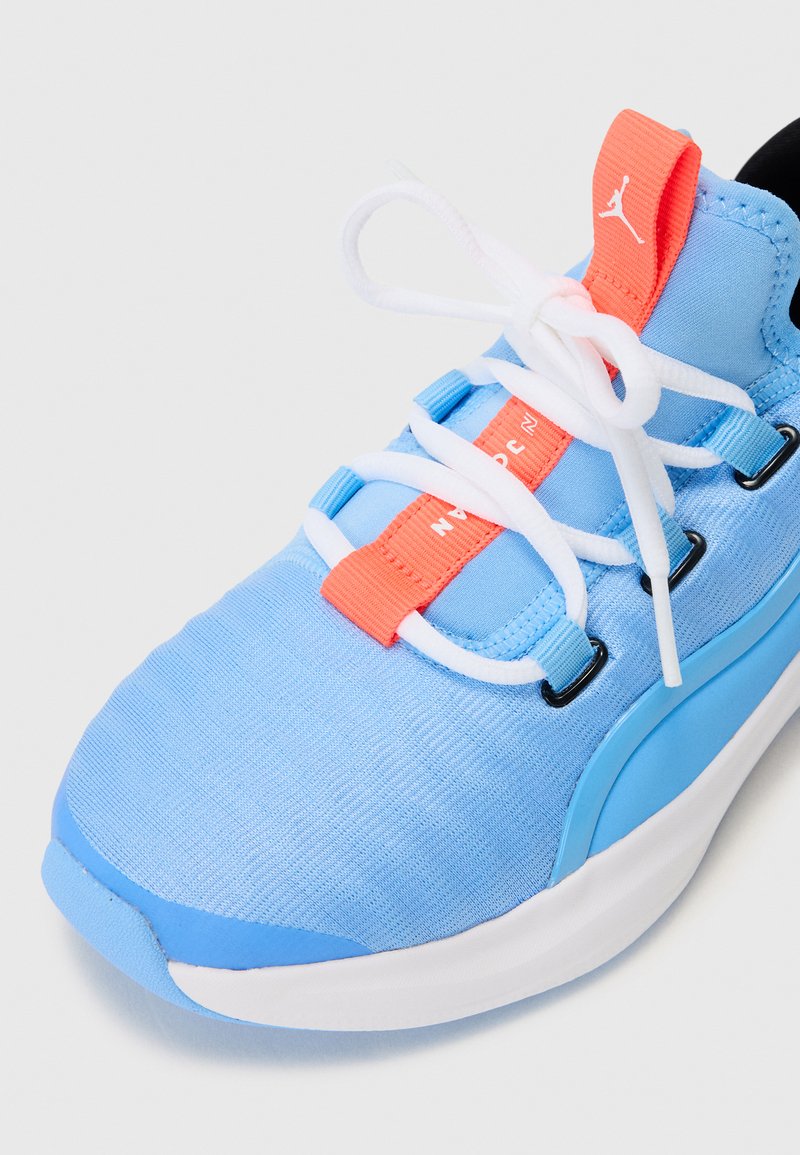 Zapatilla deportiva de color azul claro con una parte superior texturizada, cordones blancos, una etiqueta de acento naranja y una media suela blanca. Presenta un diseño aerodinámico.