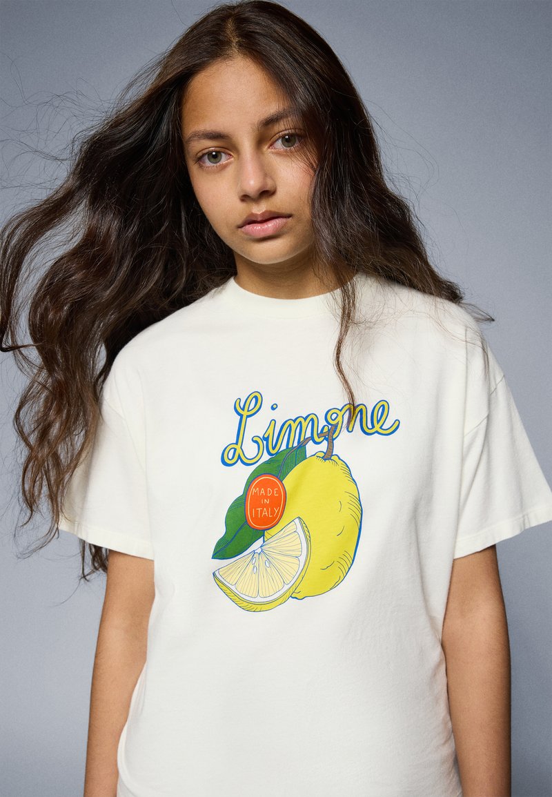 Cream-colored t-shirt featuring a lemon graphic with green leaves and a circular "Made in Italy" tag, short sleeves, and a relaxed fit.