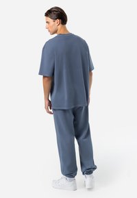 Laisvai priglundantis, trumpomis rankovėmis mėlynas marškinėliai ir derančios mėlynos kelnės su elastingais rankogaliais, derinamos su baltomis stambiais sportbačiais. Sklandus paviršius.