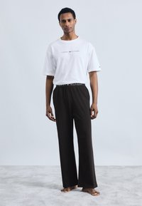 T-shirt blanc à manches courtes avec logo "TOMMY HILFIGER", associé à un pantalon ample marron avec une ceinture élastique de marque.