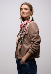 Écharpe en soie ornée d'un imprimé léopard sur un fond rose et beige, drapée élégamment autour du cou. Portée avec une veste taupe.