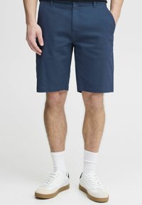 Shorts bleumarin dintr-un material neted, cu bucle pentru curea, buzunare laterale și o croială lejeră. Asortați cu adidași albi și șosete.