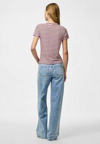 Svītraina rozā un baltā pieguļoša t-krekla kombinācija ar gaiši ziliem platā kāju džinsiem; krekls ir ar apaļu kakla izgriezumu un īsām piedurknēm.