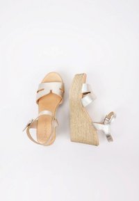 Sandalias de cuña plateadas con dos correas horizontales y un hebilla. La cuña tiene una apariencia de yute trenzado y texturizado. Interior de cuero suave.