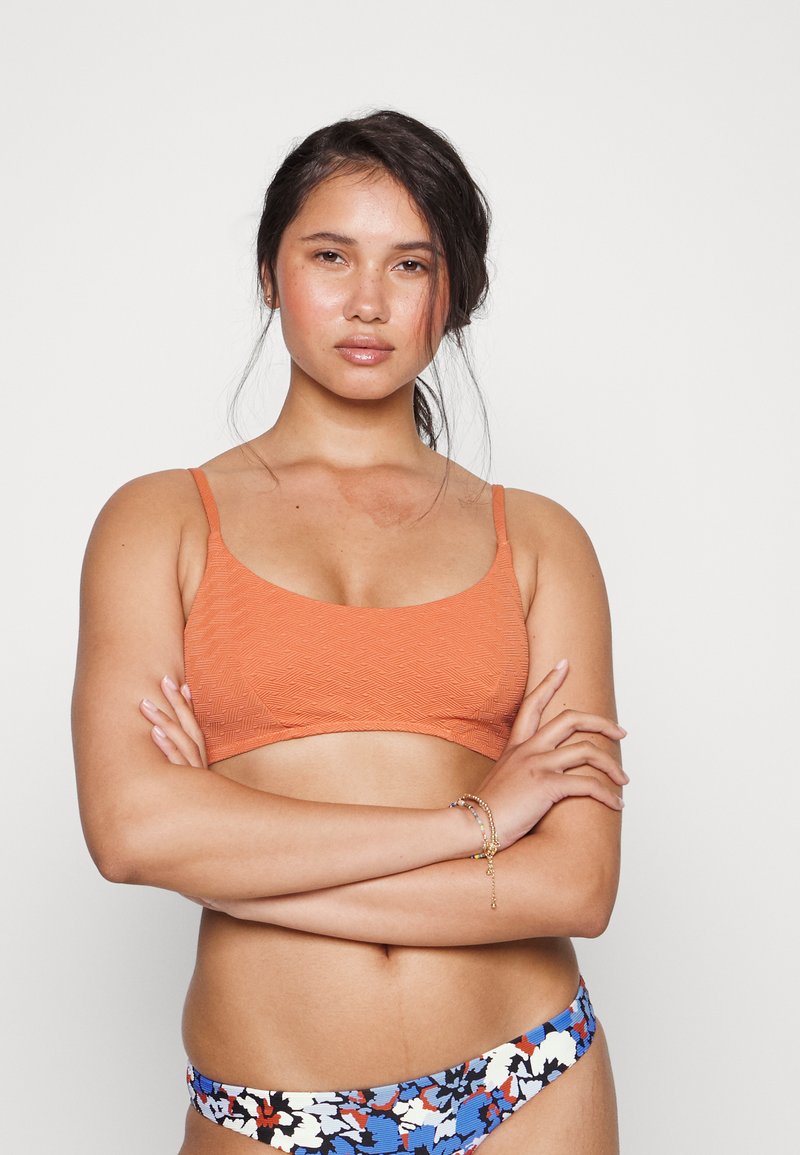 Top de biquíni laranja texturizado com alças largas, combinado com fundo de biquíni com padrão em azul, branco e design floral vermelho.