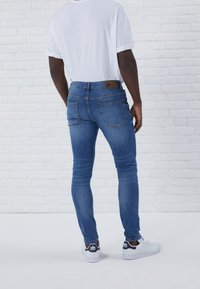 Slim-fit blå jeans med fem fickor och synliga stygn, tillsammans med en vit t-shirt med rullade ärmar och vita sneakers.