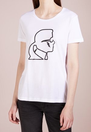 Persoon draagt een wit T-shirt met een zwarte lijntekening van een zijprofiel van een persoon met een zonnebril en een bliksemschicht op de wang.