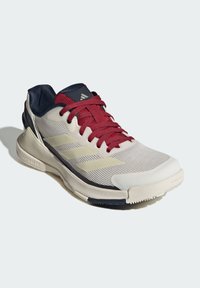 Scarpa sportiva con tomaia in mesh grigio chiaro, lacci rossi, dettagli blu navy e suola in gomma liscia con motivi in rilievo per una migliore aderenza.