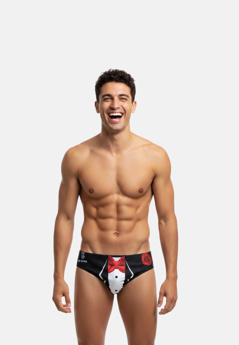 Slip de bain noir avec un design de smoking comportant une chemise blanche et un nœud papillon rouge, accentué par un graphique de rose rouge sur le côté gauche.