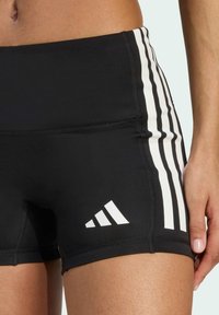 Czarne szorty sportowe z białym trój paskowym wzorem po bokach oraz akcentem logo. Wykonane z elastycznej, gładkiej tkaniny o dopasowanym kroju.