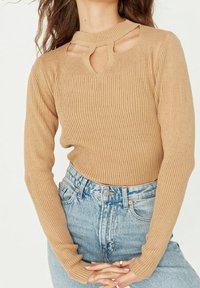 Beige geripptes Langarmshirt mit ausgeschnittenem Ausschnitt und figurbetonter Silhouette. Kombiniert mit hoch taillierten hellblauen Jeans.