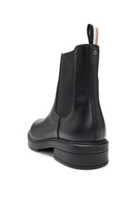 Bottine Chelsea en cuir noir avec panneau latéral élastique, languette à rayures noires et beiges, et logo « BOSS » embossé sur le talon.
