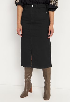 Black denim skirt with a front slit, high waist, and two pockets. Paired with knee-high brown leather boots and block heels.