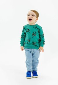Felpa verde con occhiali illustrati e un design giocoso, abbinata a jeans azzurri e sneakers blu con velcro.