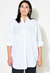 Camicia bianca oversize con bottoni, con maniche a risvolto, caratterizzata da due tasche sul petto con motivo e una texture di stoffa liscia.