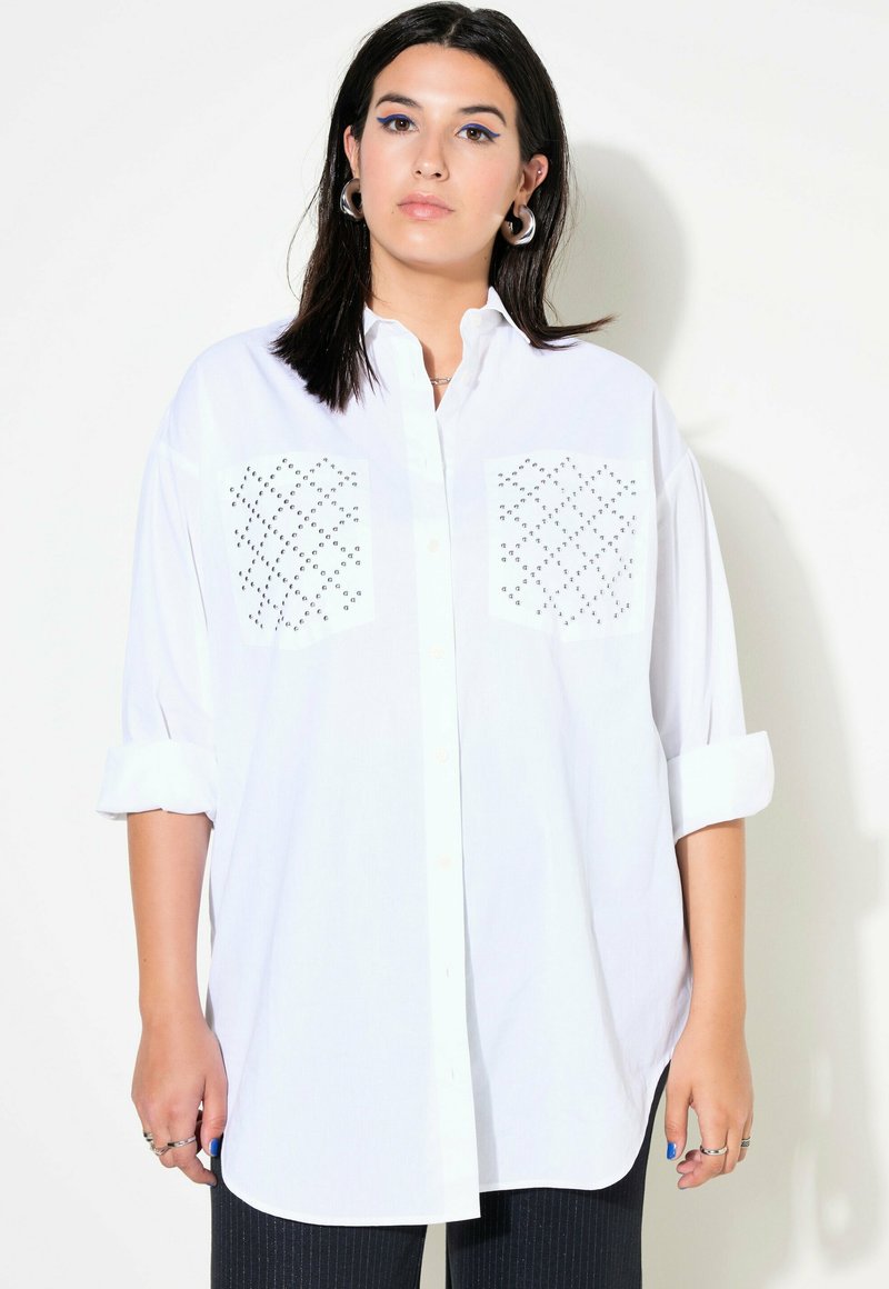 Camicia bianca oversize con bottoni, con maniche a risvolto, caratterizzata da due tasche sul petto con motivo e una texture di stoffa liscia.