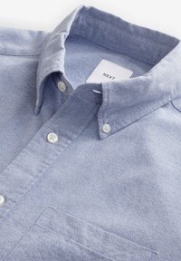 Camicia button-up azzurra realizzata in tessuto testurizzato con colletto a punta, dotata di bottoni bianchi e taschino sul petto. L'etichetta riporta la scritta "NEXT."