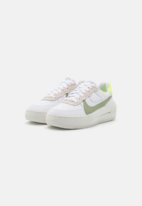 Zapatillas blancas con un swoosh verde, cordones beige y una suela texturizada. Cuello ligeramente acolchado con un acento verde neón en el talón.