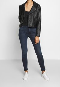 Svart läderbikerjacka, åtsittande svart linne, mörkblå tajta jeans och vita sneakers. Slät textur och enkel design.