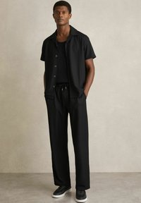 Outfit negru în două piese, compus dintr-o cămașă cu mânecă scurtă și închidere cu nasturi și pantaloni cu șnur, având o textură ribbed și o croială lejeră.
