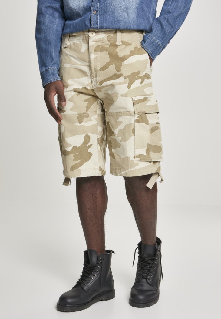Beige kamouflage cargoshorts med flera fickor, tillverkade av bomull. Kombineras med svarta snörskor, mot en neutral bakgrund.