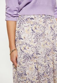 Bloemenrok met een lila en gele print, gemaakt van een soepel stof en met een elastische tailleband, gecombineerd met een lichtpaarse trui.