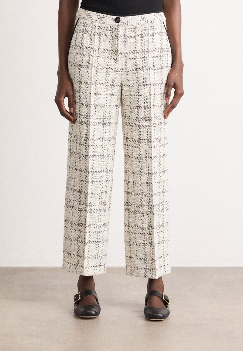 Pantaloni a vita alta larghi in tweed crema con motivo a quadri neri, indossati con scarpe nere con fibbia, mostrati dalla vita ai piedi.