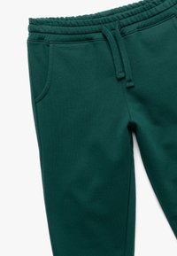 Grønne sweatpants lavet af blødt stof, med elastisk talje og snøre, sidelommer og en glat tekstur.