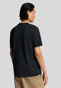 Maglietta in cotone nera con maniche corte e colletto a girocollo. Il retro presenta un design minimal con un orlo leggermente curvo.