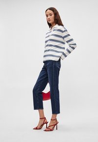 Λευκό πουκάμισο με μακριά μανίκια και ναυτικό οριζόντιο ρίγες, συνδυασμένο με σκούρα μπλε κοντά τζιν και κόκκινες σανδάλια με λεπτά λουράκια και ψηλό τακούνι.